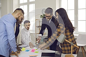 Business team writes notes on colored sticky stickers while discussing a startup project.