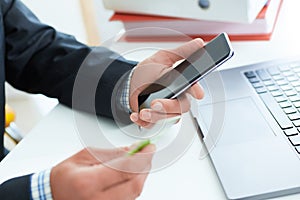 Male hands holding smart phone and credit card at office. Business, technology, cash free and internet people concept -