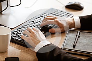 Business and technology concept. Businessman& x27;s sits at office table with hands lying on desktop computer keyboard