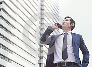 Business, technology and people concept - serious businessman with smartphone talking over office building