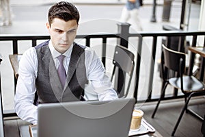 Business, technology and people concept - young man with a laptop and coffee cup at city street cafe