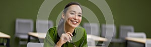 Business training. Young happy woman, female office worker sitting at desk in the office and smiling, listening to coach