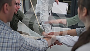 business training, young male speaker gathers hands of working team in circle raise and lower then clap each other