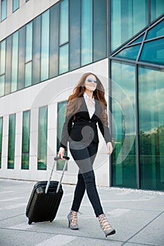 Business travel - woman with suitcase walks outside airport building