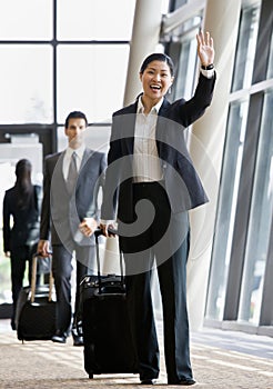 Business traveler pulling suitcase and waving