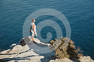 Business travelling and dream job concept. Woman in headphones holding laptop and suitcase. Seascape on background.