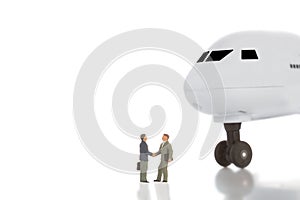 Business trip or agreement and success concept. Two miniature businessmen shaking hands near airplane ir aircraft on whit