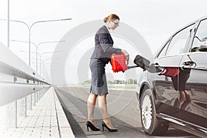 Businesswoman with canister fueling car on road against sky photo
