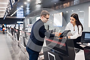 Business trip. Handsome young businessman in suit holding his passport and talking to woman at airline check in counter photo