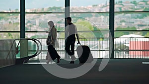 Business trip, man and woman walking to escalator in airport, carrying luggage