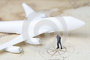 Business trip planning or travel concept, miniature adult businessman looking at compass on vintage world map with toy