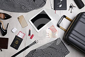 Business trip stuff and suitcase on light wooden surface, flat lay