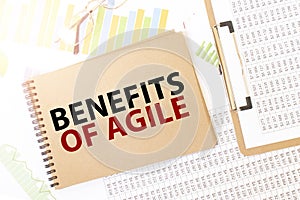 Business up graph on a sheet of craft colour Notepad with BENEFITS OF AGILE sign. Notepad on desk with financial documentation