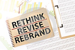 Business up graph on a sheet of craft colour Notepad with RETHINK REVISE REBRAND sign. Notepad on desk with financial