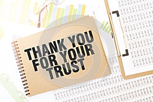 Business up graph on a sheet of craft colour Notepad with THANK YOU FOR YOUR TRUST. sign. Notepad on desk with financial