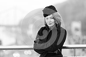 Business winter dress code for every day. Woman standing near of bridge barrier in black coat. Portrait of lady in black