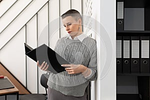 Business woman accountant with a short haircut stands in the office with a folder for business papers