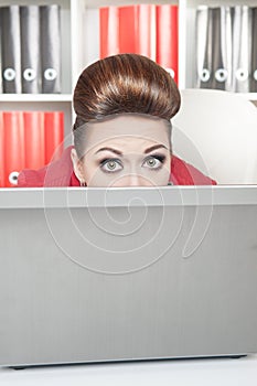 Business woman afraid and hiding behind the computer