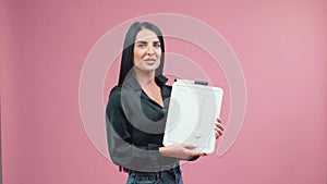 Business woman in black blouse with white tablet in her hands is posing isolated on pink background