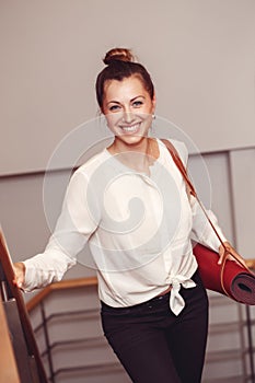 Business woman with blue eyes in white blouse shirt and black pants holding, carrying yoga mat in office