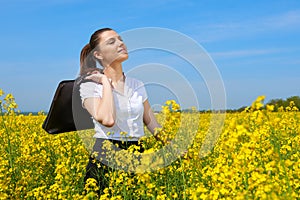 Business woman with briefcase relaxing in flower field outdoor under sun. Young girl in yellow rapeseed field. Beautiful spring la