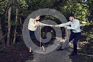 Business woman and business man pulling rope in the city park in formal wear