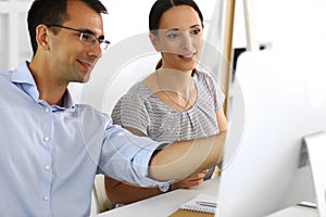 Business woman and businessman discussing questions while using a computer in modern office. Group of diverse people