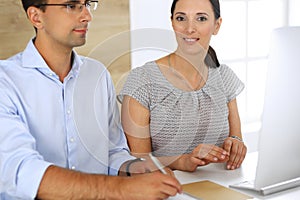 Business woman and businessman discussing questions while using a computer in modern office. Group of diverse people