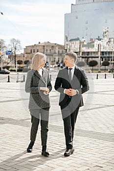 A business woman and a businessman are walking around the city outside the office, planning and discussing a new project