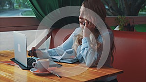 Business woman in a cafe talking on cell phone writing in dairy