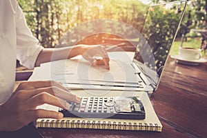 Business woman calculate and analyzing graph document financial with laptop vintage tone.