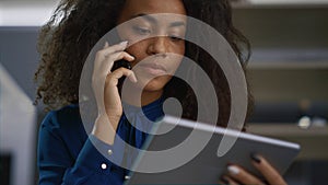 Business woman calling phone in workplace. African american worker using tablet.