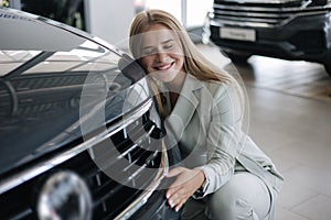 Business woman chossing a new car in a car showroom. Happy female hug new car and very glad. Elegant female in suit