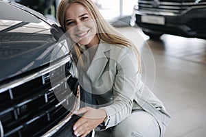 Business woman chossing a new car in a car showroom. Happy female hug new car and very glad