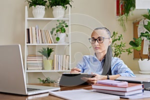 Business woman with clipboard sitting at workplace, looking talking at computer screen