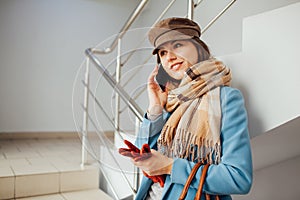 Business woman in coat stands on the stairs in the mall with smartphone. Shopping. Fashion