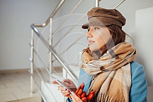 Business woman in coat stands on the stairs in the mall with smartphone. Shopping. Fashion