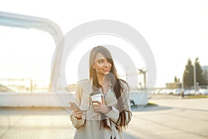 Business woman with coffee and talking on the phone near office. Portrait of beautiful smiling female with phone, standing outdoor