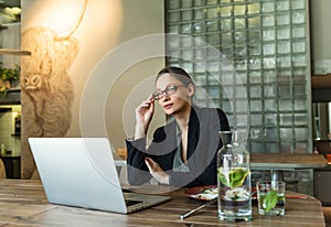 Business Woman with cup of coffee and laptop at table in a cafe. Focused business woman in stylish glasses sit on cafe working on