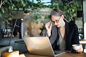 Business Woman with cup of coffee and laptop at table in a cafe. Focused business woman in stylish glasses sit on cafe working on