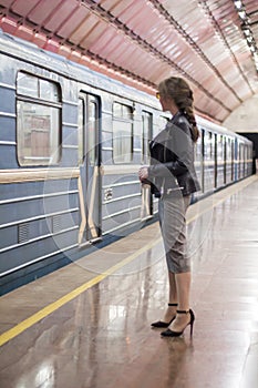 Business woman with a cup of coffee at subway station and train. Beautiful girl in sunglasses and a jacket at the subway station.