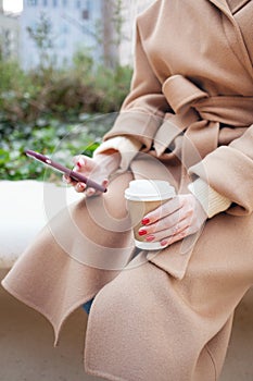 Business woman is drinking coffee on the street while having break. Close-up of hands with take away coffee. Reading news, e-mail