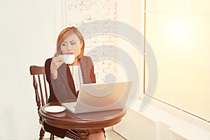 Business woman drinking coffee and using laptop in office