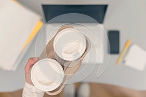 Business woman drinks coffee from paper cups while working on the laptop in an office.