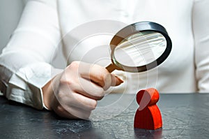 Business woman examines a red man`s figure through a magnifying glass. Analysis of the personal qualities of the employee.