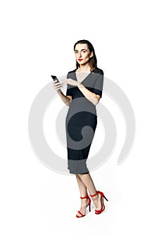 Business woman fatal woman in a black dress with red lipstick looks to the camera holding a smartphone, isolated on a white