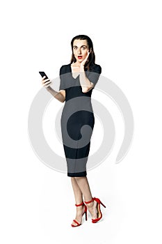 Business woman fatal woman in a black dress with red lipstick looks to the camera holding a smartphone, isolated on a white