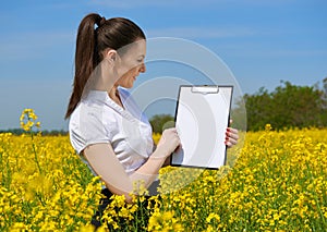 Business woman in flower field outdoor look on clipboard. Young girl in yellow rapeseed field. Beautiful spring landscape, bright