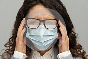 Business woman with foggy glasses from breath caused by wearing disposable mask on studio grey wall