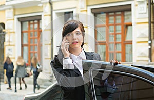Business-woman gets into the car and talks on cell phone